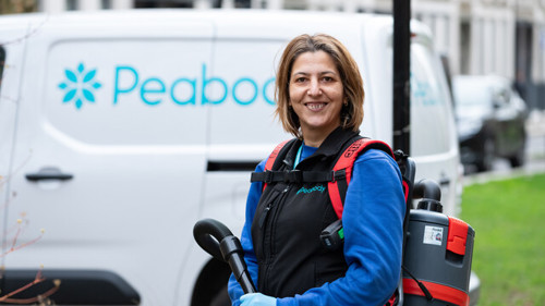 A smiling, female Peabody colleague with shoulder-length brown hair, wearing a portable hoover like a backpack standing in front of a white Peabody-branded van.