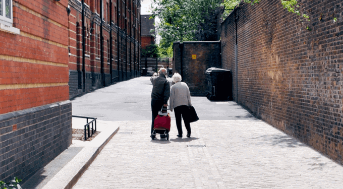 Two people walking outside on a path, next to red buildings