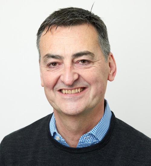 Headshot of a man in a dark grey jumper, smiling