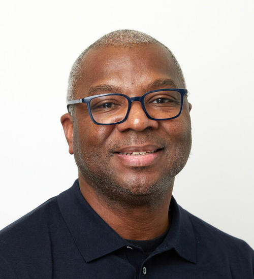 Headshot of a man in a dark blue shirt and glasses, smiling