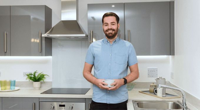 Man wearing a light blue short sleeved shirt, standing in a kitchen