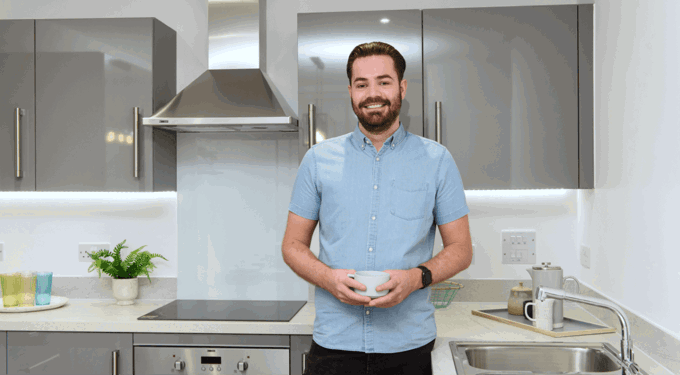 Man wearing a light blue short sleeved shirt, standing in a kitchen