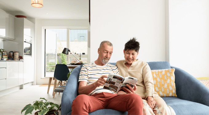 Two people sitting on a light blue sofa looking at a magazine